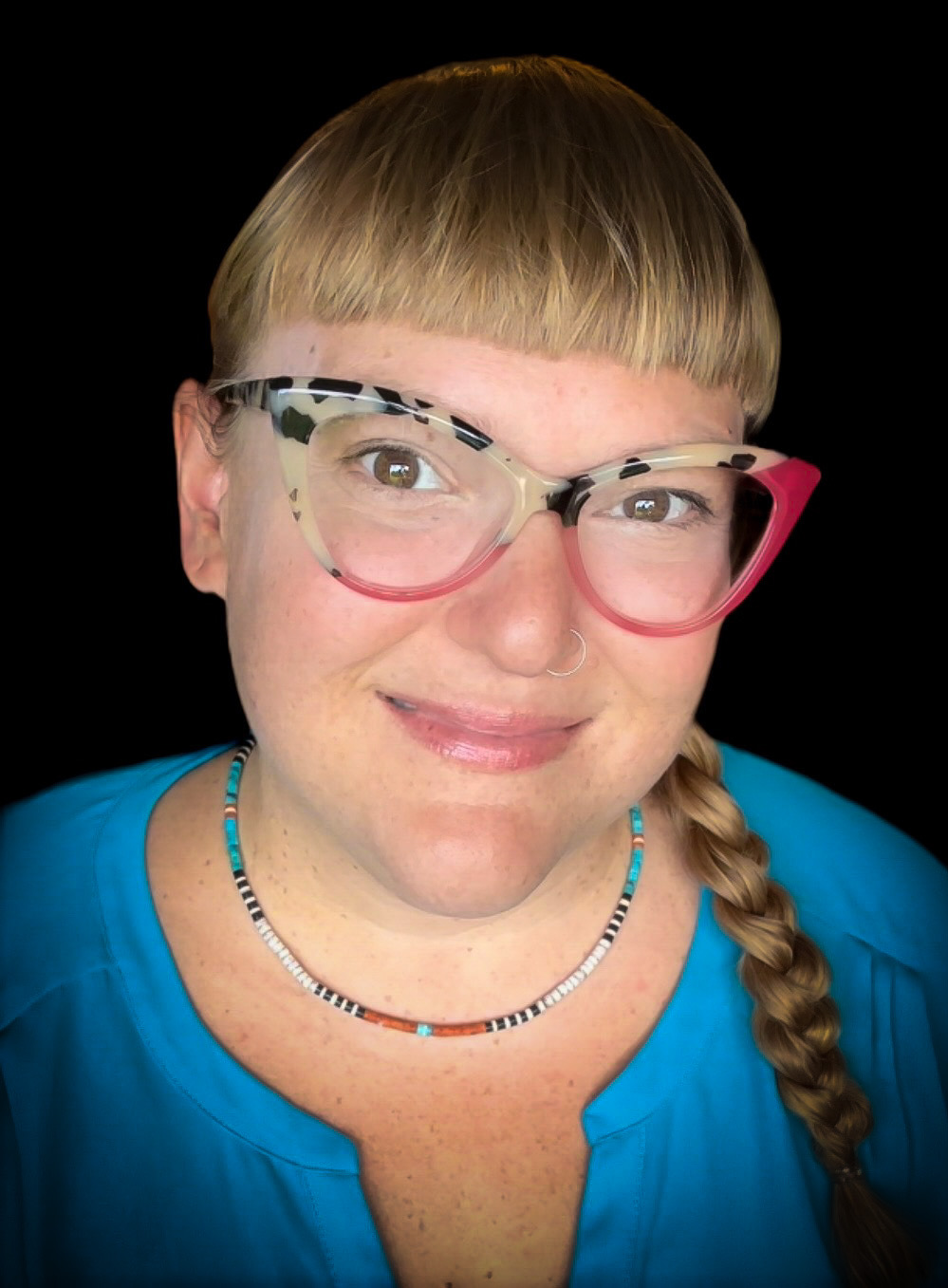 Headshot of myself with a dark background. I am wearing pink glasses and a blue shirt.